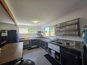 A compact kitchen with a built-in oven, a microwave, and a sink. There is a window providing natural light, and a shelf with dishes.