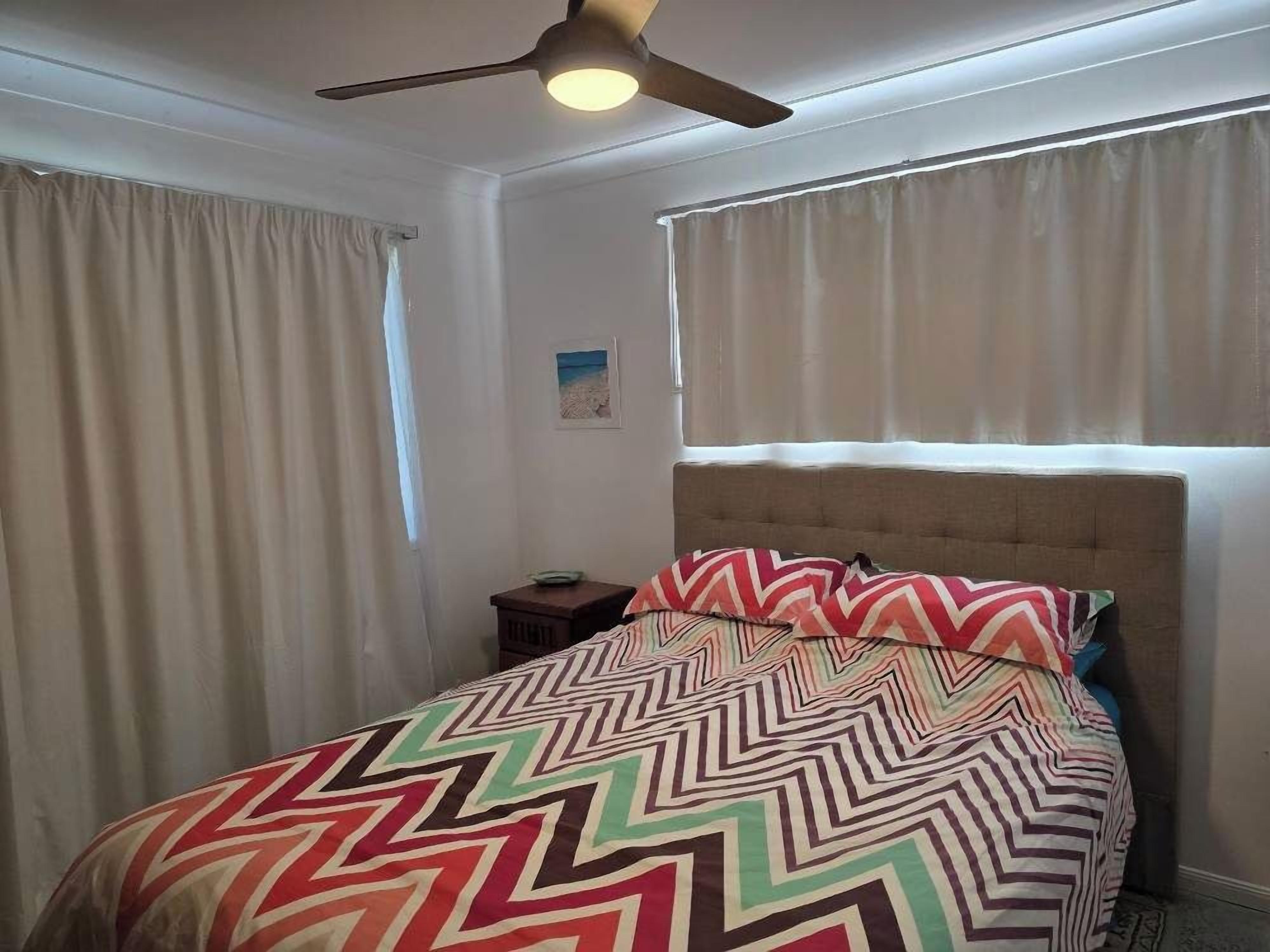 A bedroom with a bed, a ceiling fan, and a window with curtains.
