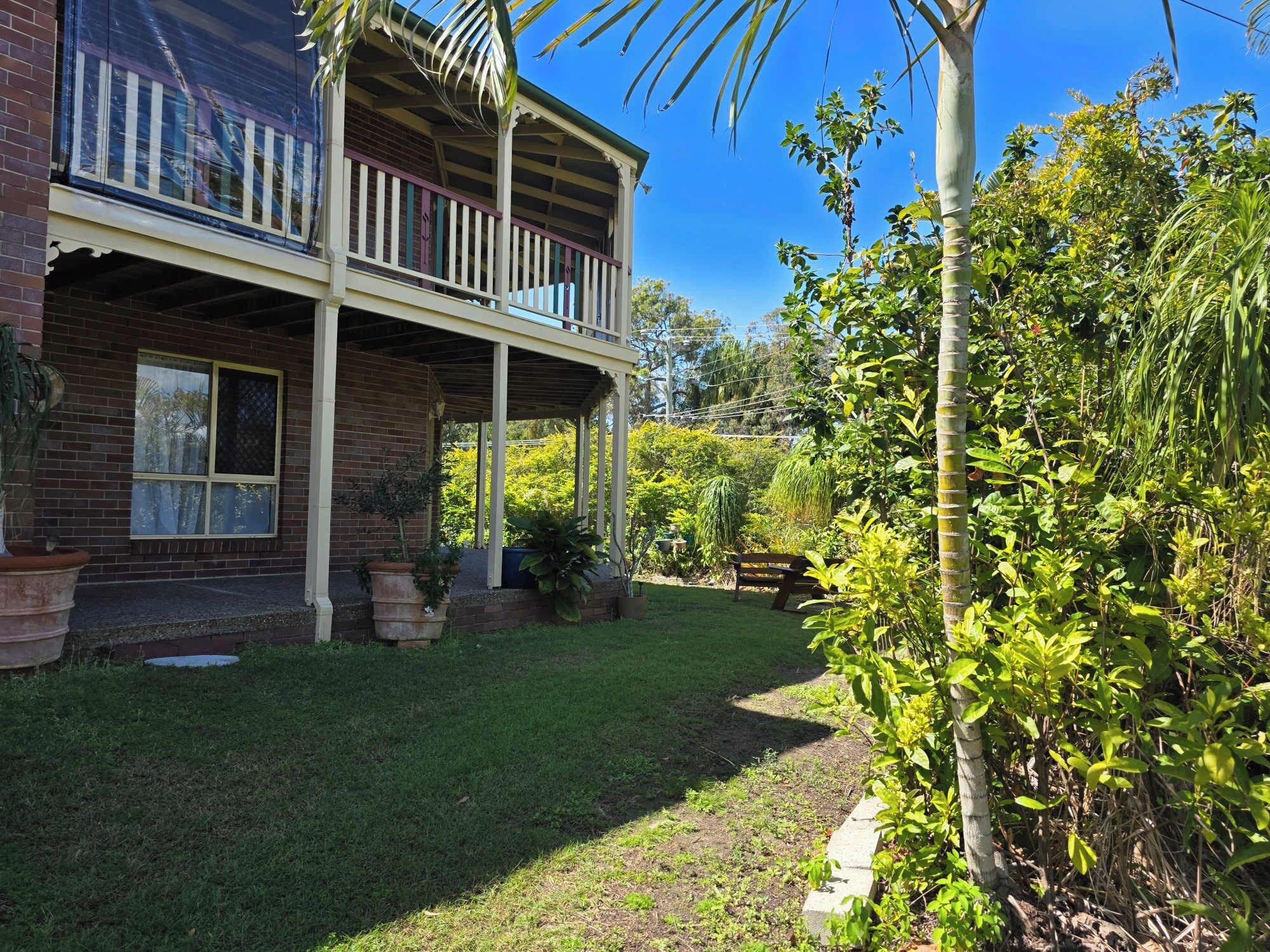 A two-story house with a balcony, surrounded by lush greenery and a well-maintained lawn.