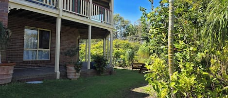 A two-story house with a balcony, surrounded by lush greenery and a well-maintained lawn.