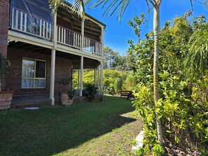 A two-story house with a balcony, surrounded by lush greenery and a well-maintained lawn.