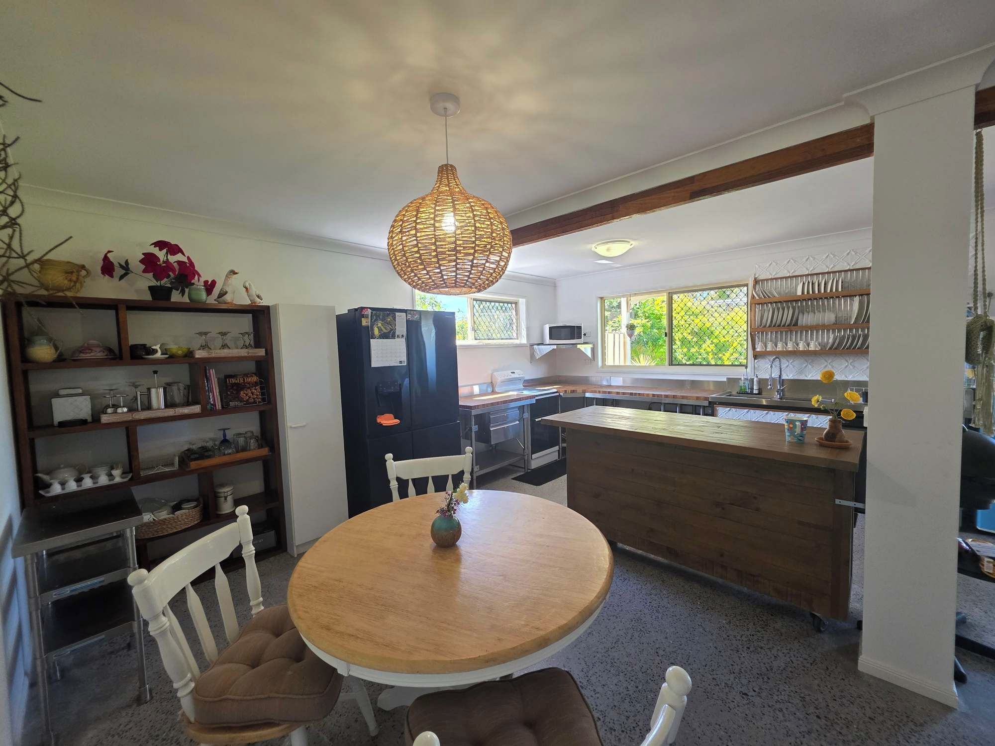 A kitchen with a round wooden table, white chairs, a black refrigerator, and a hanging light fixture.