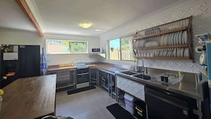 A compact kitchen with a built-in oven, a microwave, and a sink. There is a window providing natural light, and a shelf with dishes. - SoKo Holiday Apartment (Agnes Water)