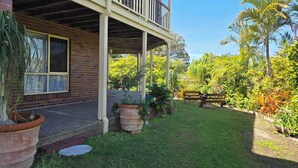 A two-story house with a covered porch, brick exterior, and a well-maintained garden with various plants and a wooden fence. - SoKo Holiday Apartment (Agnes Water)