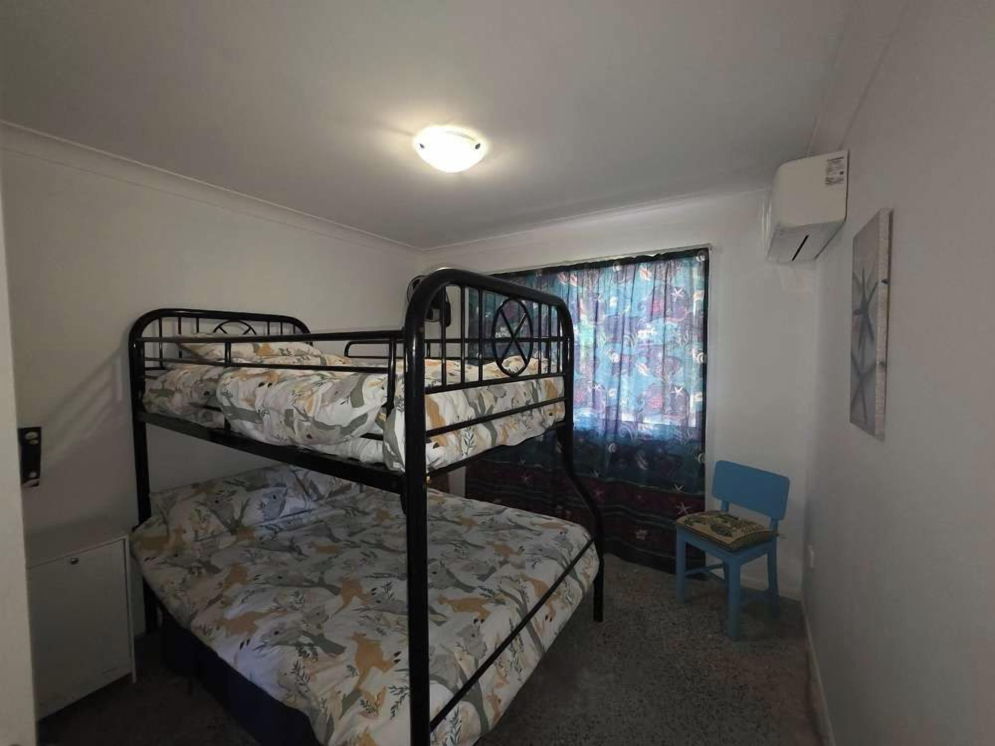 A room with a bunk bed, a small desk, a chair, and a window with curtains.