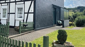 Una casa tradicional con entramado de madera y una extensión moderna, un camino de entrada pavimentado y una cerca verde.