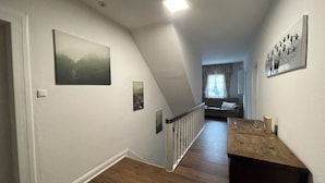 Un pasillo con piso de madera, una escalera y una sala de estar al fondo.