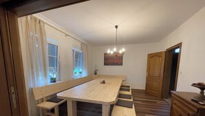 Un comedor con una mesa de madera larga, bancos y una araña.