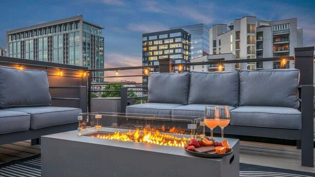 A rooftop terrace with a glass-top fire pit, grey sofas, and a glass table with fruit and a drink. - Music Row - Luxury Home w/ 5 en-suites! (Nashville)