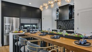 A modern kitchen with dark cabinetry, stainless steel appliances, and a wooden dining table set for six. - Music Row - Luxury Home w/ 5 en-suites! (Nashville)