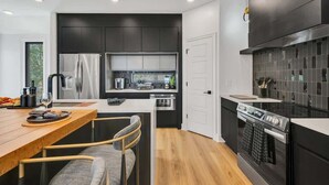 A modern kitchen with dark cabinetry, stainless steel appliances, and a wooden dining table with chairs. - Music Row - Luxury Home w/ 5 en-suites! (Nashville)