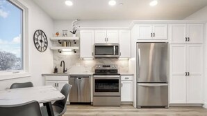 A modern kitchen with white cabinets, stainless steel appliances, a marble countertop, and a dining area with a table and chairs.