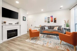 Un salon moderne avec une cheminée, un téléviseur à écran plat, un canapé gris agrémenté de fauteuils orange et une table basse.