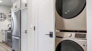 A laundry room with stacked washers and dryers, a refrigerator, and a clock on the wall.