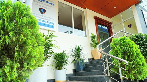 A hotel entrance with a staircase, potted plants, and a sign for Crystal Homes. - Sweet Crystal Homes C V Raman Nagar (Bengaluru)