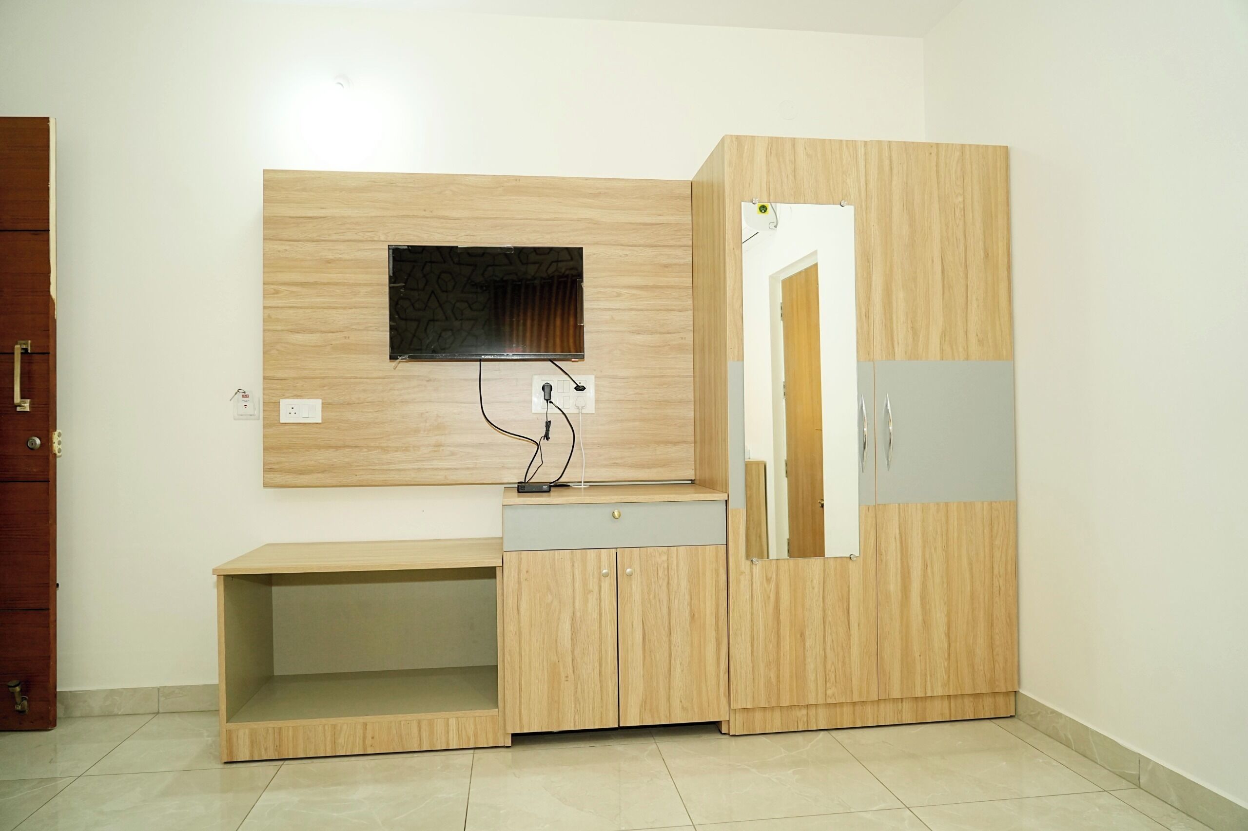 A room with a wooden cabinet, a TV mounted on the wall, and a door.