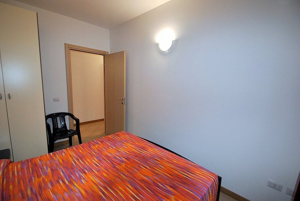 A small room with a bed, a chair, a wardrobe, and a door.
