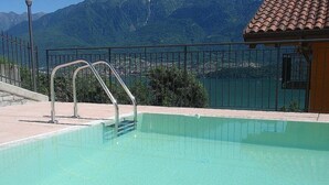 A swimming pool with a metal ladder, surrounded by a fence, with a mountain view in the background.