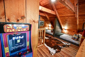 A cozy cabin with a Pac-Man arcade game, a bunk bed, and a cowhide rug.