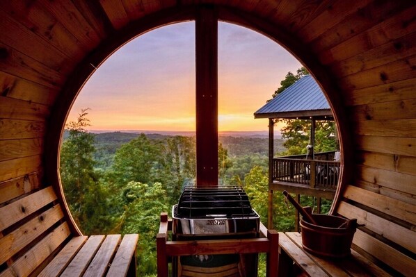 A wooden cabin with a circular window overlooking a forested landscape at sunset.
