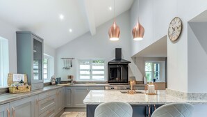 A modern kitchen with grey cabinetry, a large island with bar stools, pendant lighting, and a black range hood.