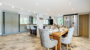 A spacious kitchen with a large dining table, grey upholstered chairs, and a built-in oven.