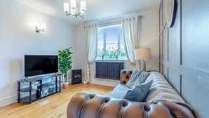 A modern living room with a leather sofa, a flat-screen TV, a potted plant, and a window with curtains.