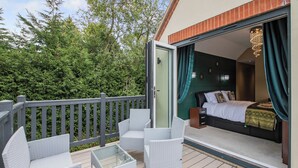 A balcony with wicker furniture, a glass table, and a bed with a dark headboard.