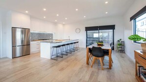 Eine moderne Küche mit einem Edelstahl-Kühlschrank, einer zentralen Kochinsel mit Barhocker und einem Essbereich mit Holztisch und Stühlen.