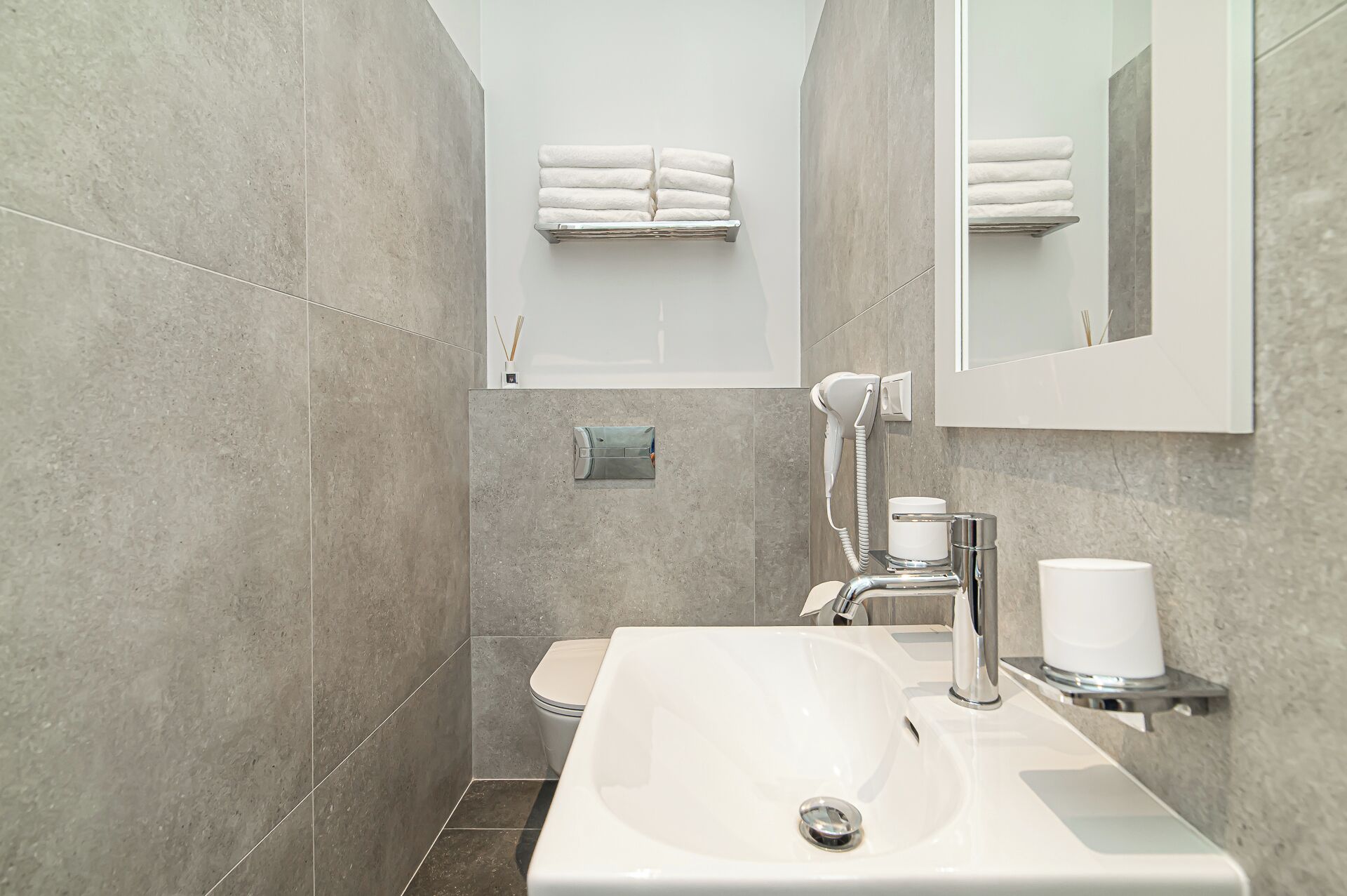 A modern bathroom with a white sink, a handheld showerhead, and a towel rack with neatly folded towels.