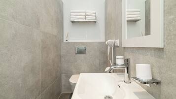 A modern bathroom with a white sink, a handheld showerhead, and a towel rack with neatly folded towels.