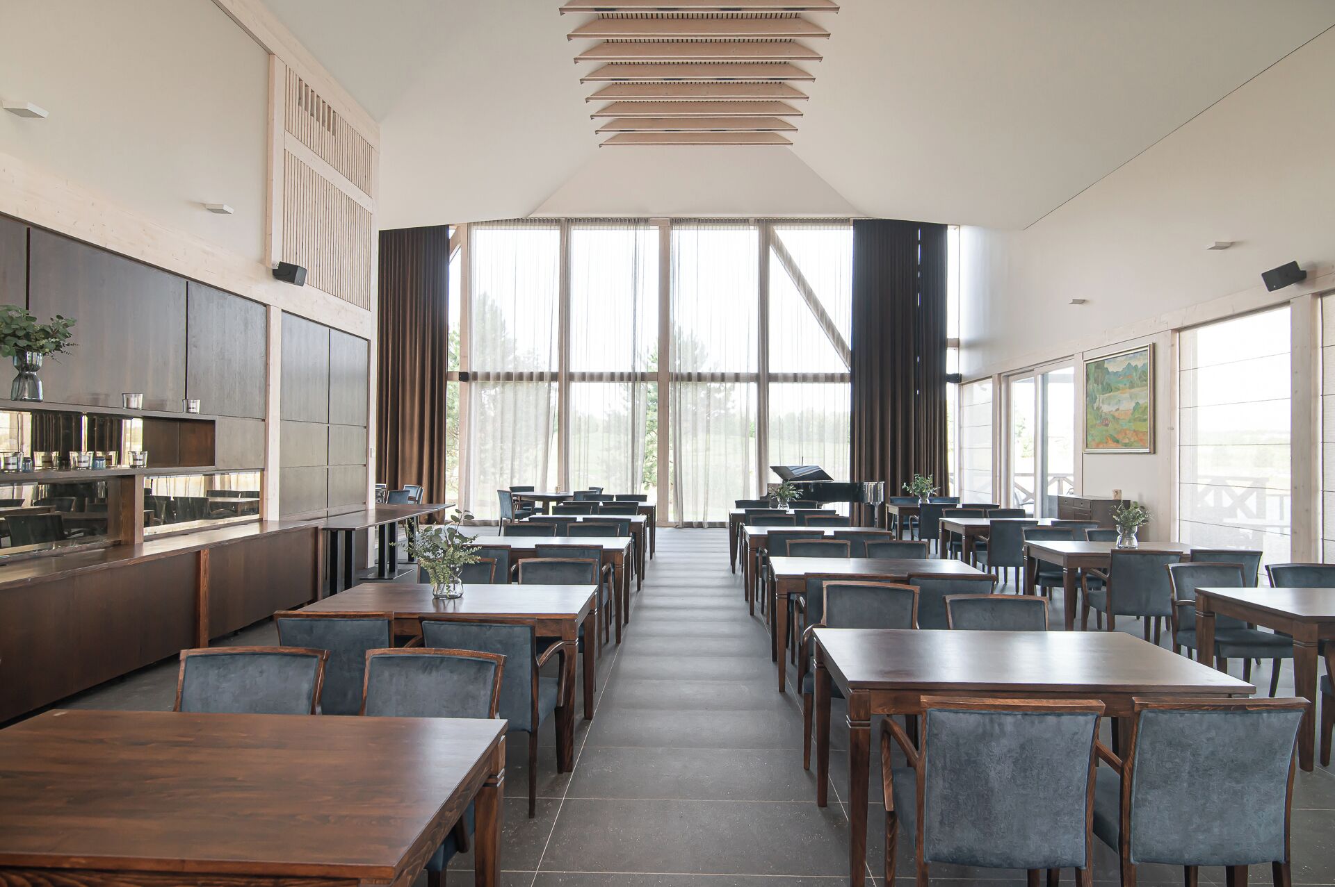 A spacious dining area with high ceilings, large windows, and modern furniture.