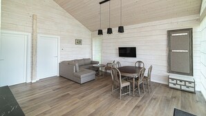 Un'ampia zona giorno con soffitto in legno, un divano grigio, un tavolo da pranzo con sedie e un televisore montato a parete.