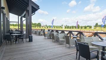 A covered outdoor seating area with tables and chairs, overlooking a golf course.