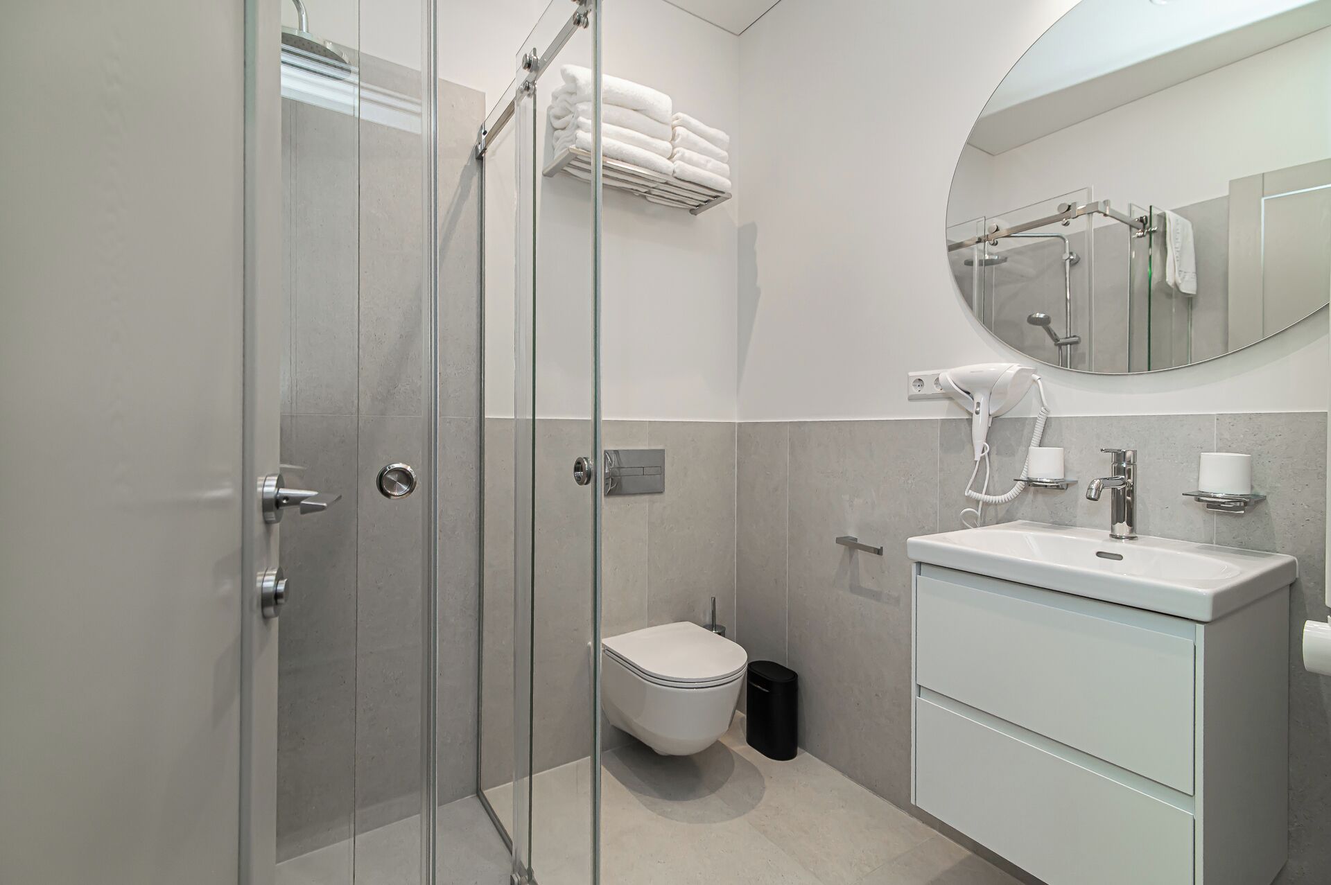 Un baño moderno con cabina de ducha de vidrio, inodoro, lavamanos con espejo y toallero.