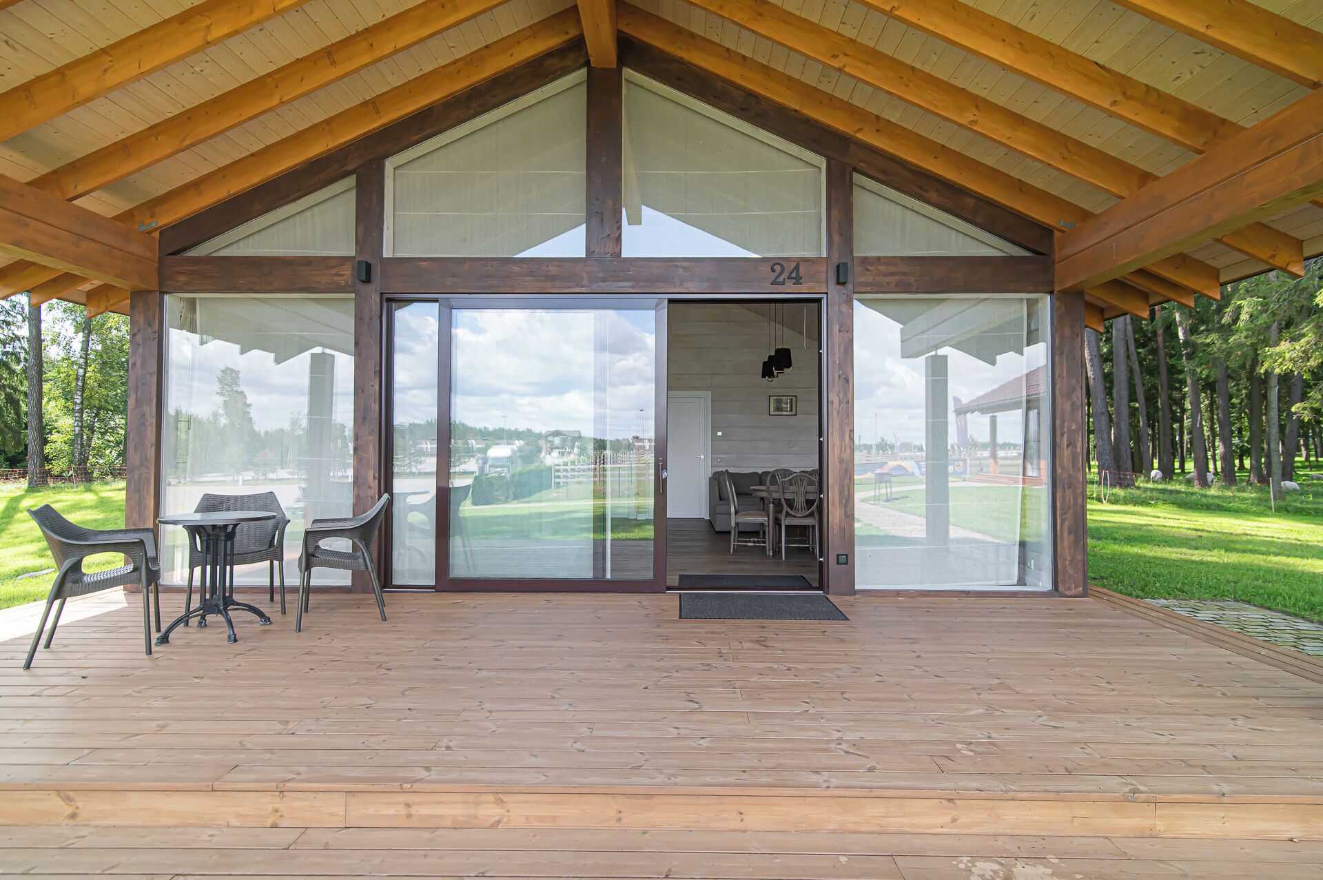 A covered outdoor area with a wooden deck, a glass door leading to a room with a sofa and table, and a view of a golf course.