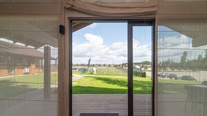 Vista dall'interno di un edificio attraverso una porta vetrata che si apre su un'area esterna con un patio in legno e un prato.