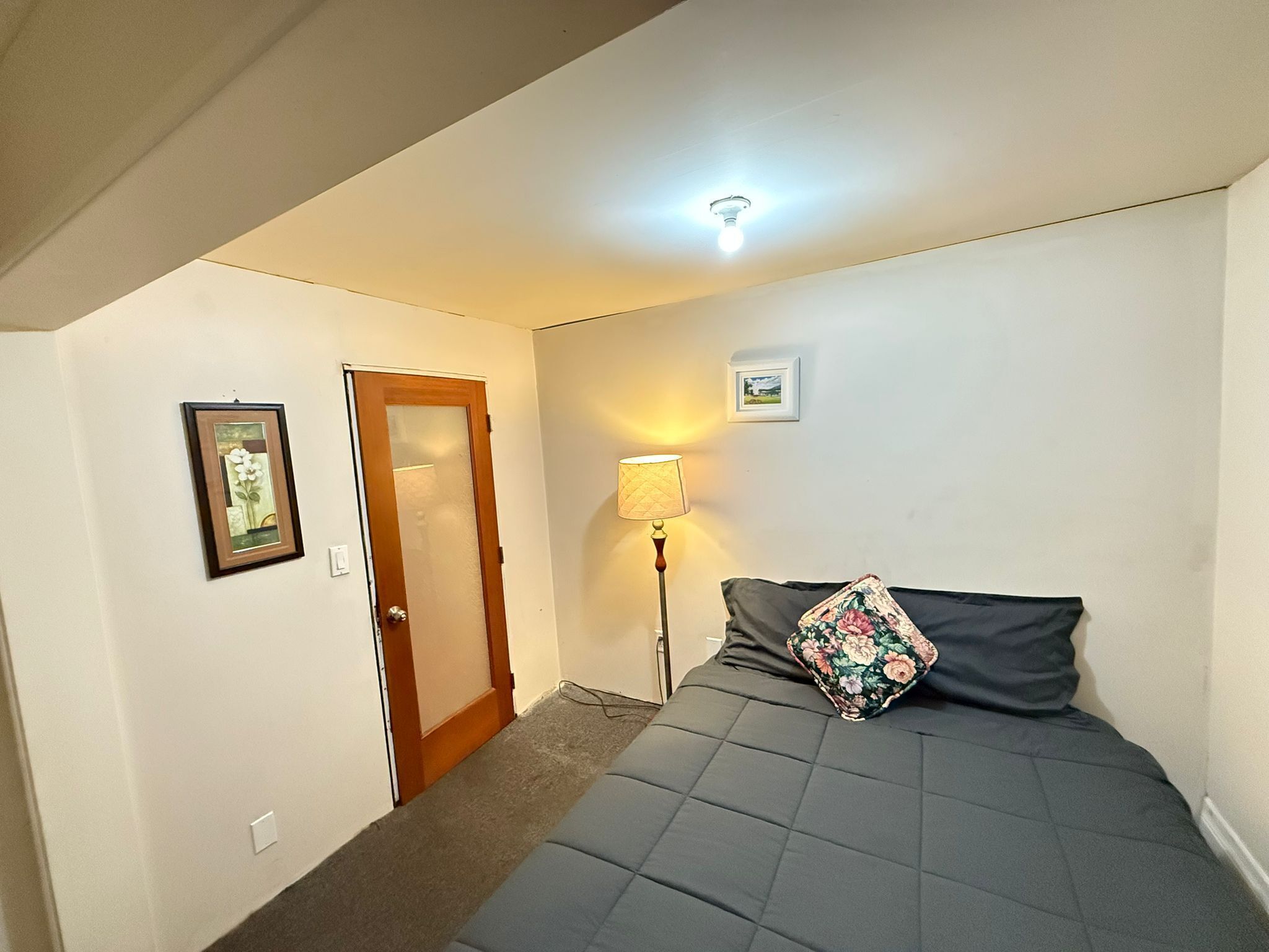 Une chambre à coucher avec un lit, une porte, une lampe et un tableau encadré au mur.