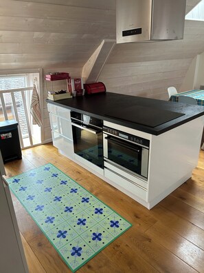 A modern kitchen with a black countertop, double ovens, and a stainless steel range hood.