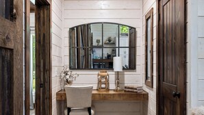Une petite pièce au décor rustique, comprenant un bureau en bois, une chaise, une lampe et une fenêtre donnant sur une cuisine.