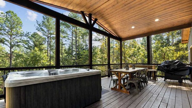 Une terrasse en bois avec un jacuzzi, des sièges d’extérieur et une vue sur une forêt.