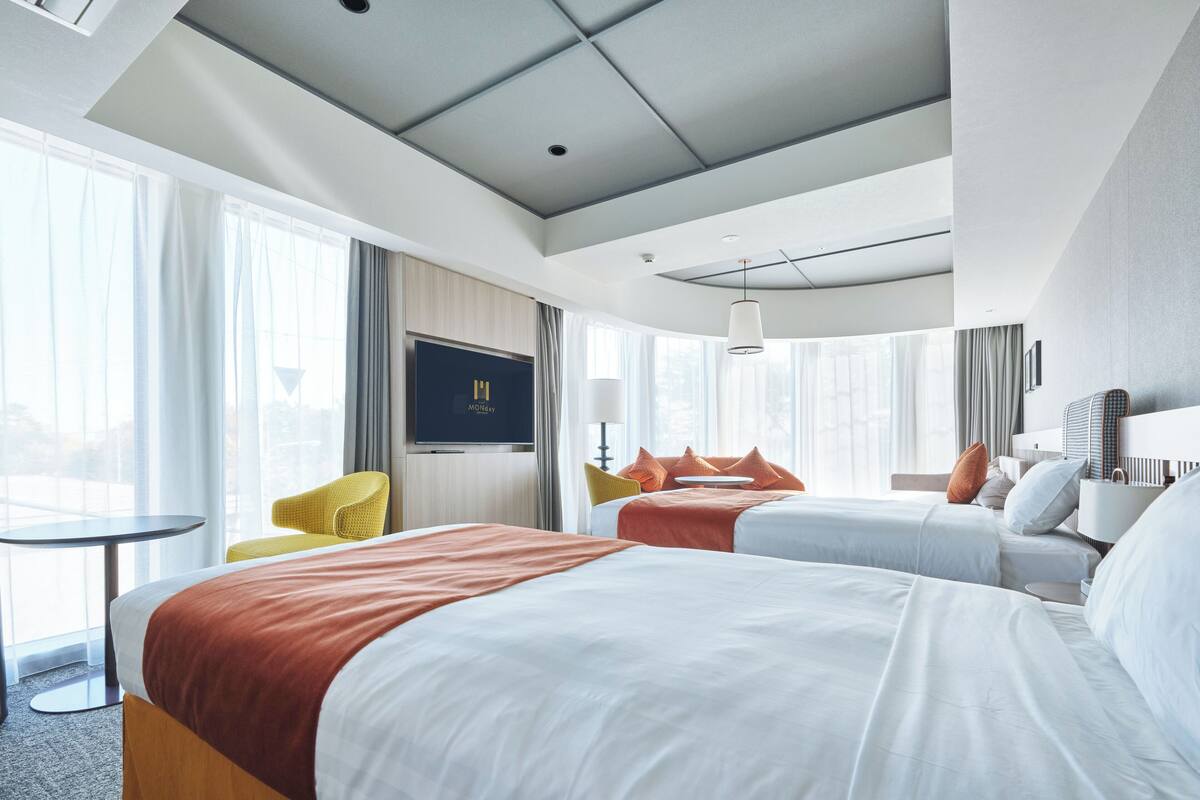 A hotel room with a large bed, a smaller bed, a sofa, a TV, and a window with curtains.