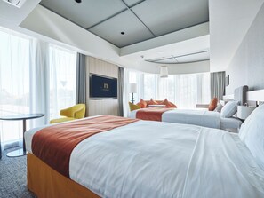 A hotel room with a large bed, a smaller bed, a sofa, a TV, and a window with curtains.
