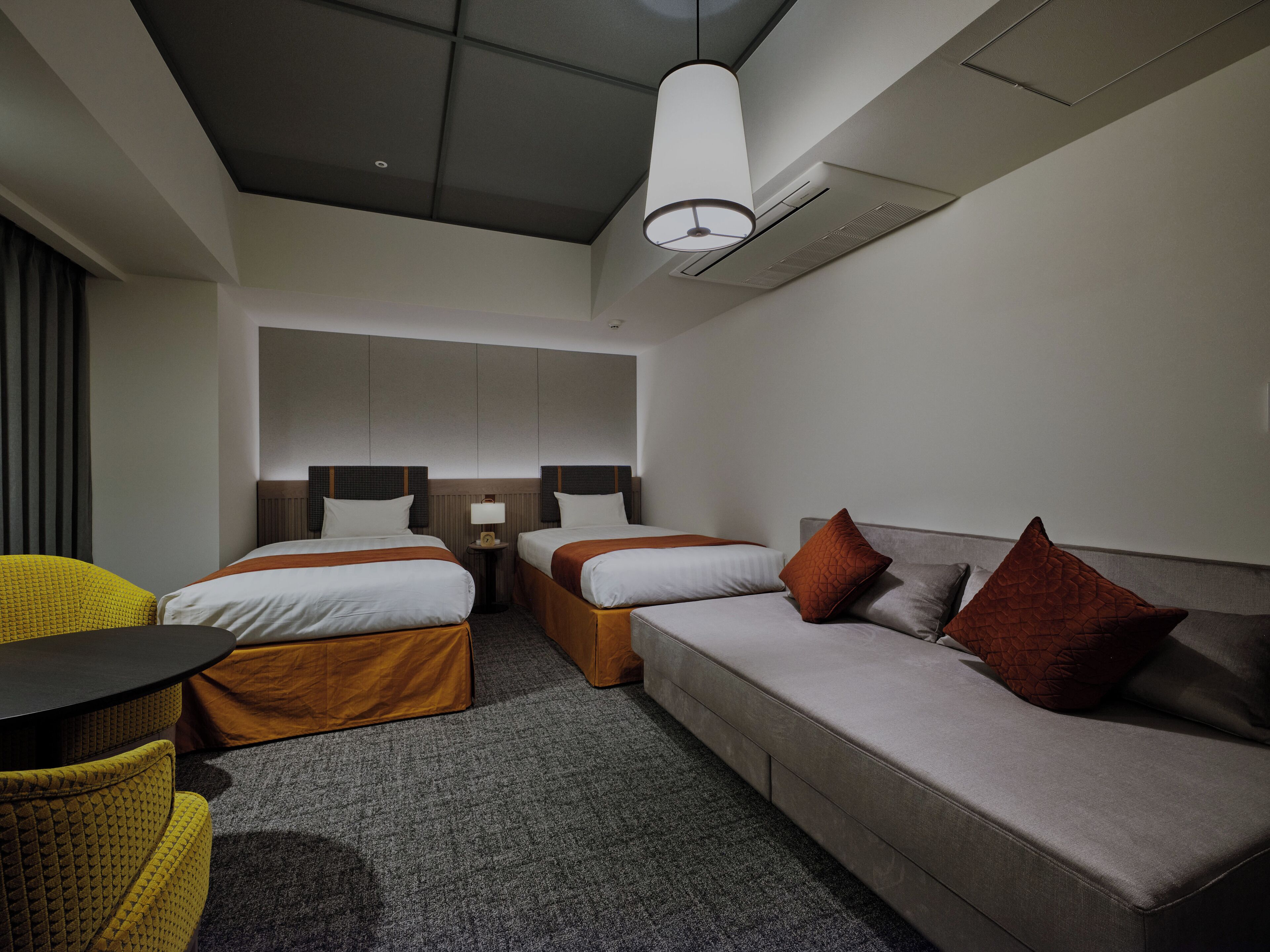 Une chambre d’hôtel avec deux lits simples, un canapé, une petite table et une chaise.