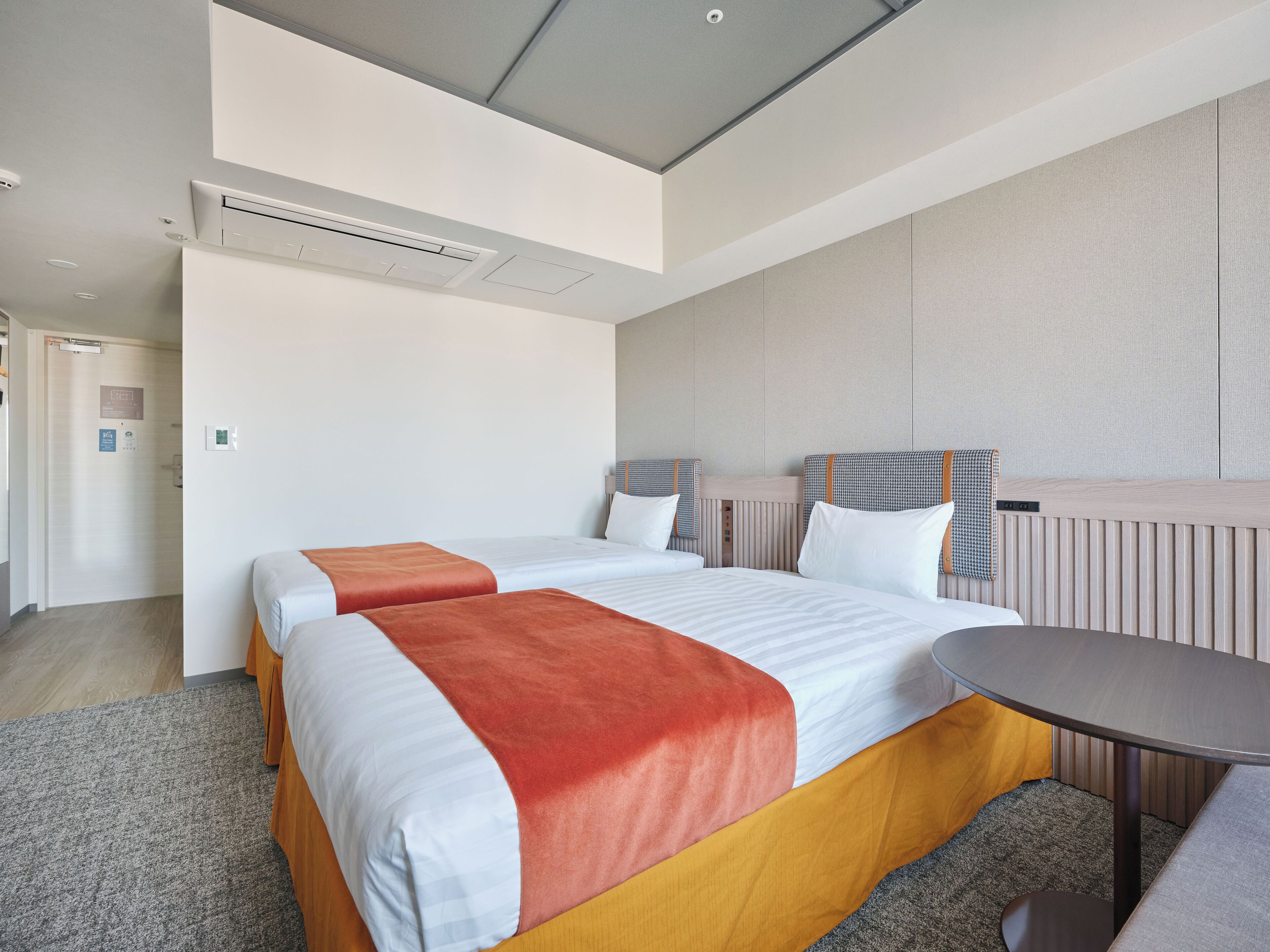 A hotel room with two beds, a round table, and a built-in bench.