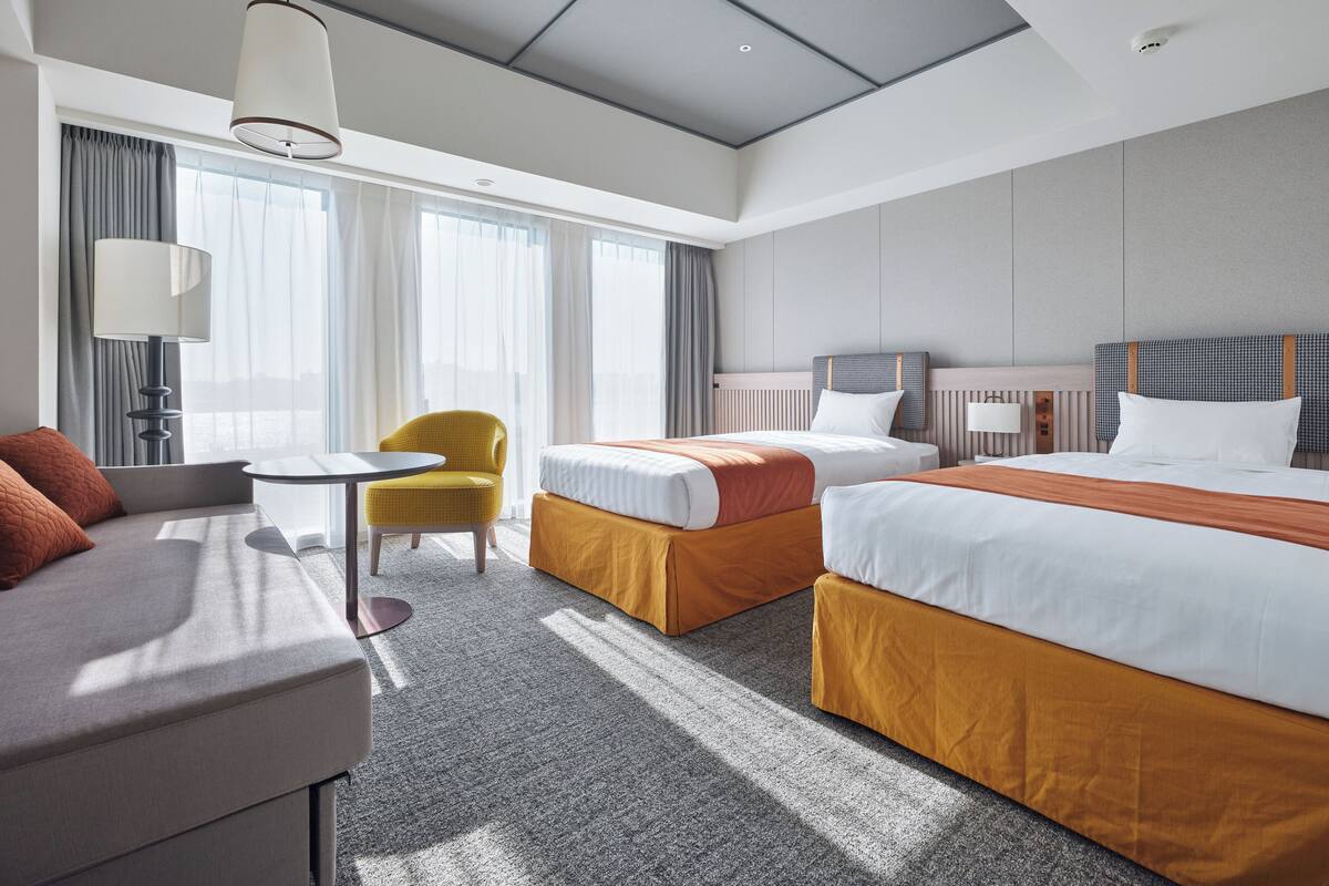A hotel room with a bed, a sofa, a chair, a small table, and a lamp.