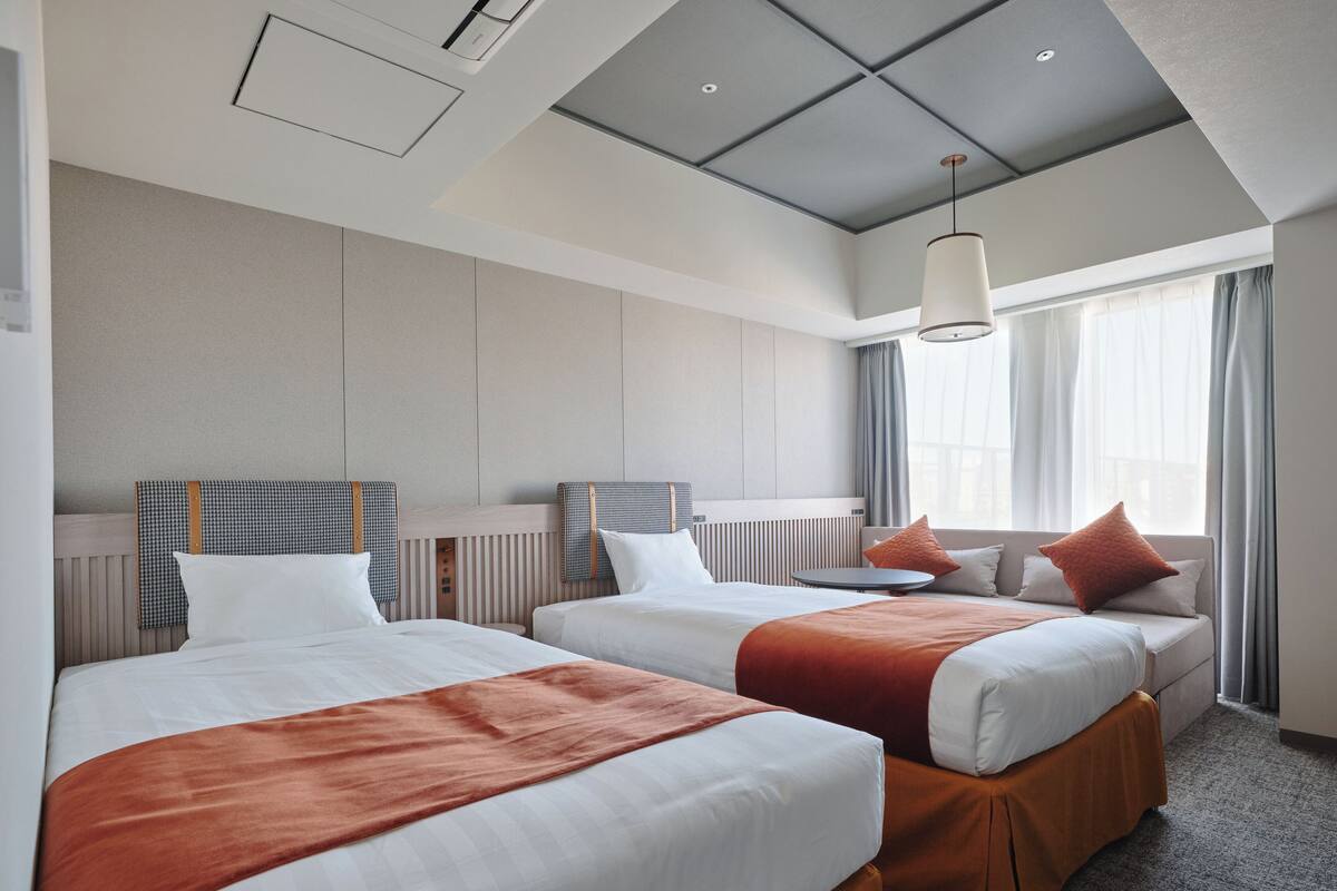 A hotel room with two beds, a round table, and a large window with curtains.