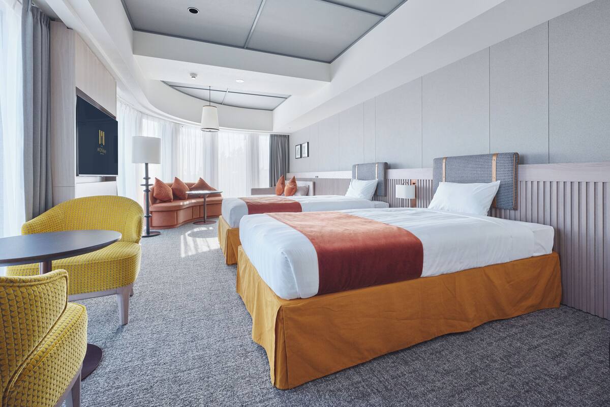 A modern hotel room with a large bed, two bedside tables, a sofa, and a small round table.