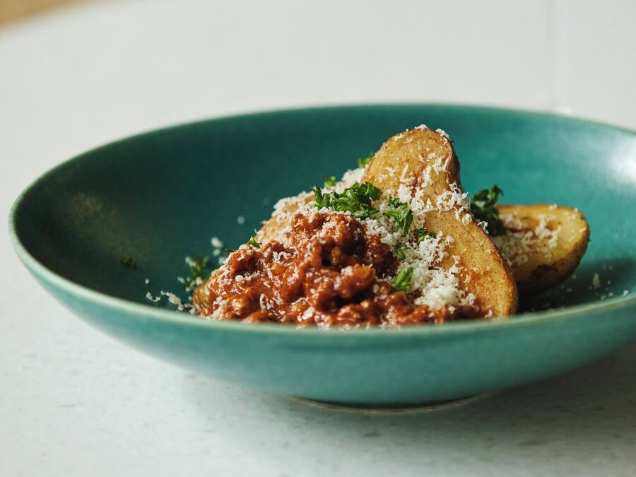A teal bowl with a pasta dish, a fork, and a glass of white wine on a table.