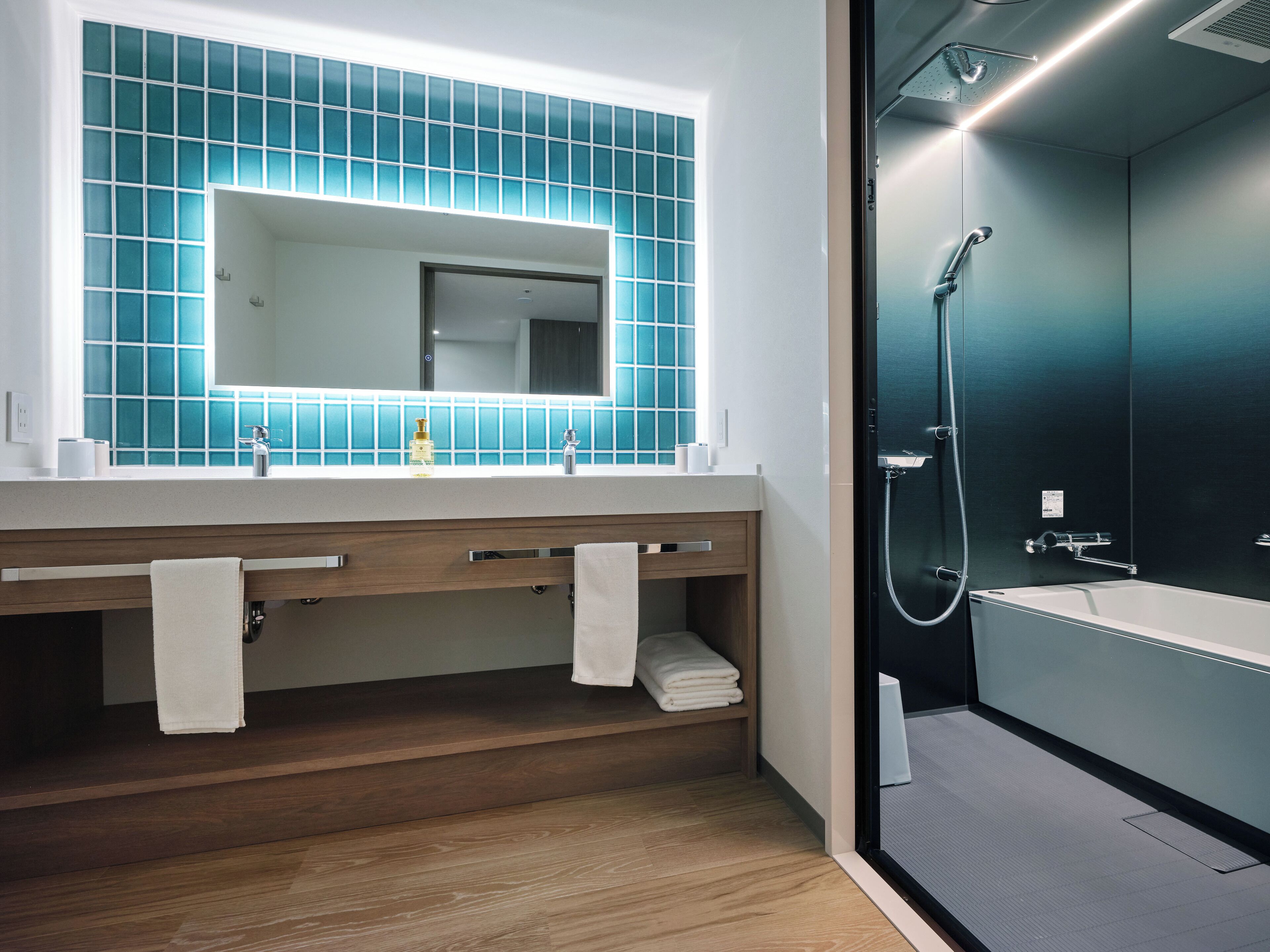 A modern bathroom with a large mirror, two sinks, a shower, and a wooden vanity.